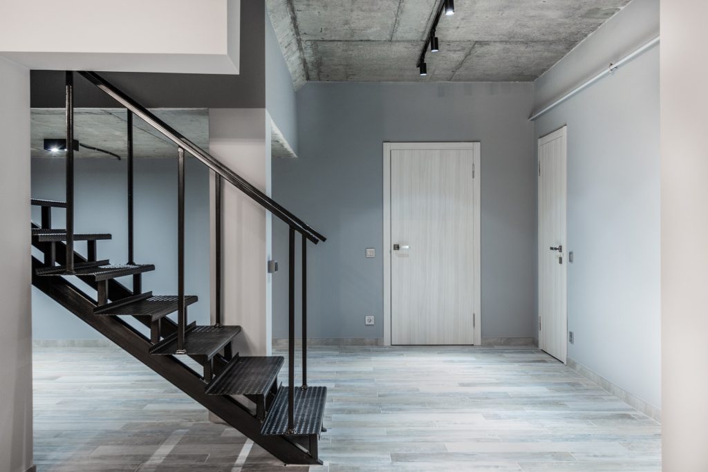 Black stairway with railing located in corridor of modern light spacious apartment with doors and laminate floor and glowing lamps